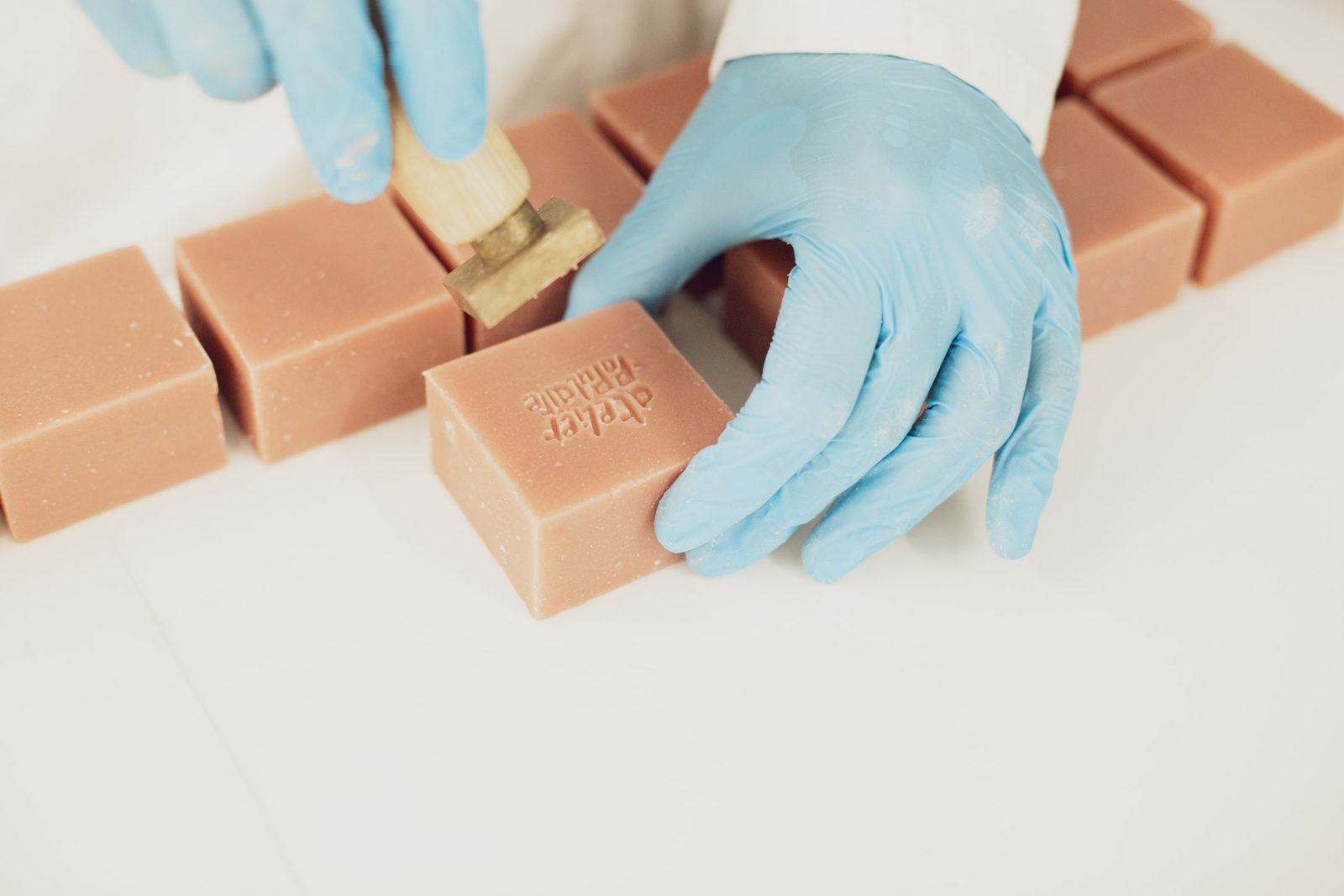Des mains gantées de bleu tamponnent un pavé de savon